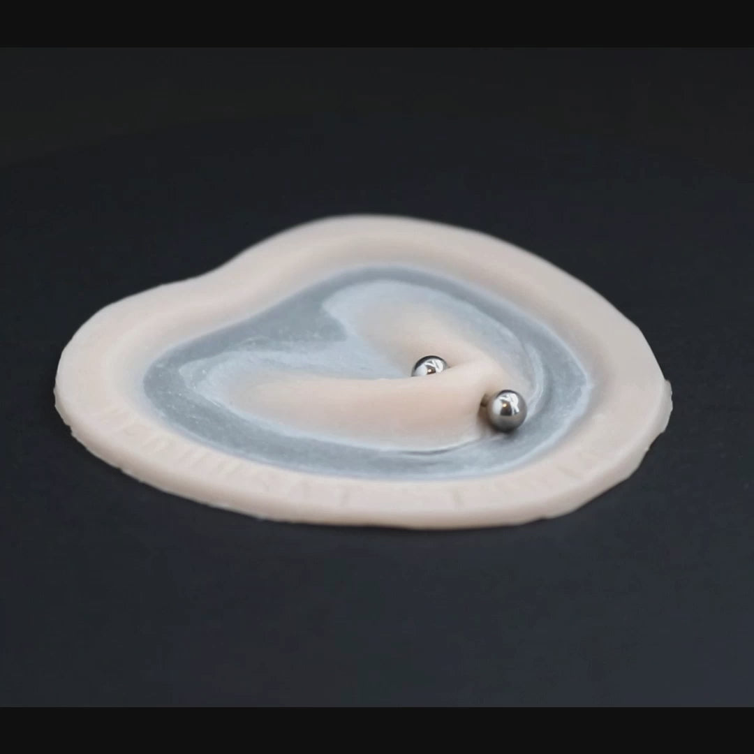 Stretched piercing prosthetic in vanilla shade on a black turntable, slowly rotating.