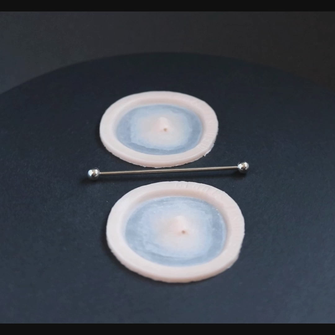 Two silicone patches in vanilla shade and a steel piercing rod on a black turntable, slowly rotating.
