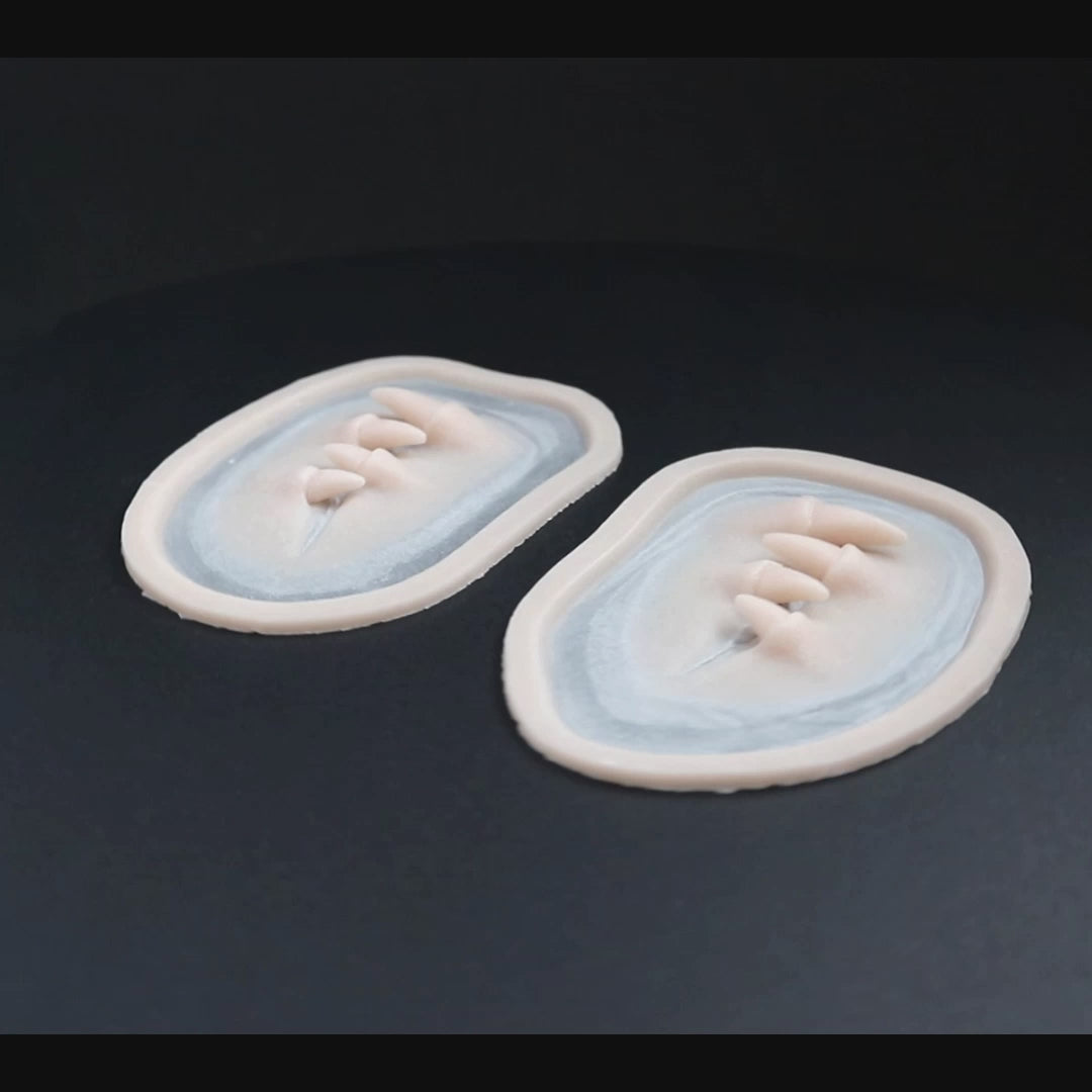 A pair of Facial Fangs prosthetics in vanilla shade on a black turntable, slowly rotating.