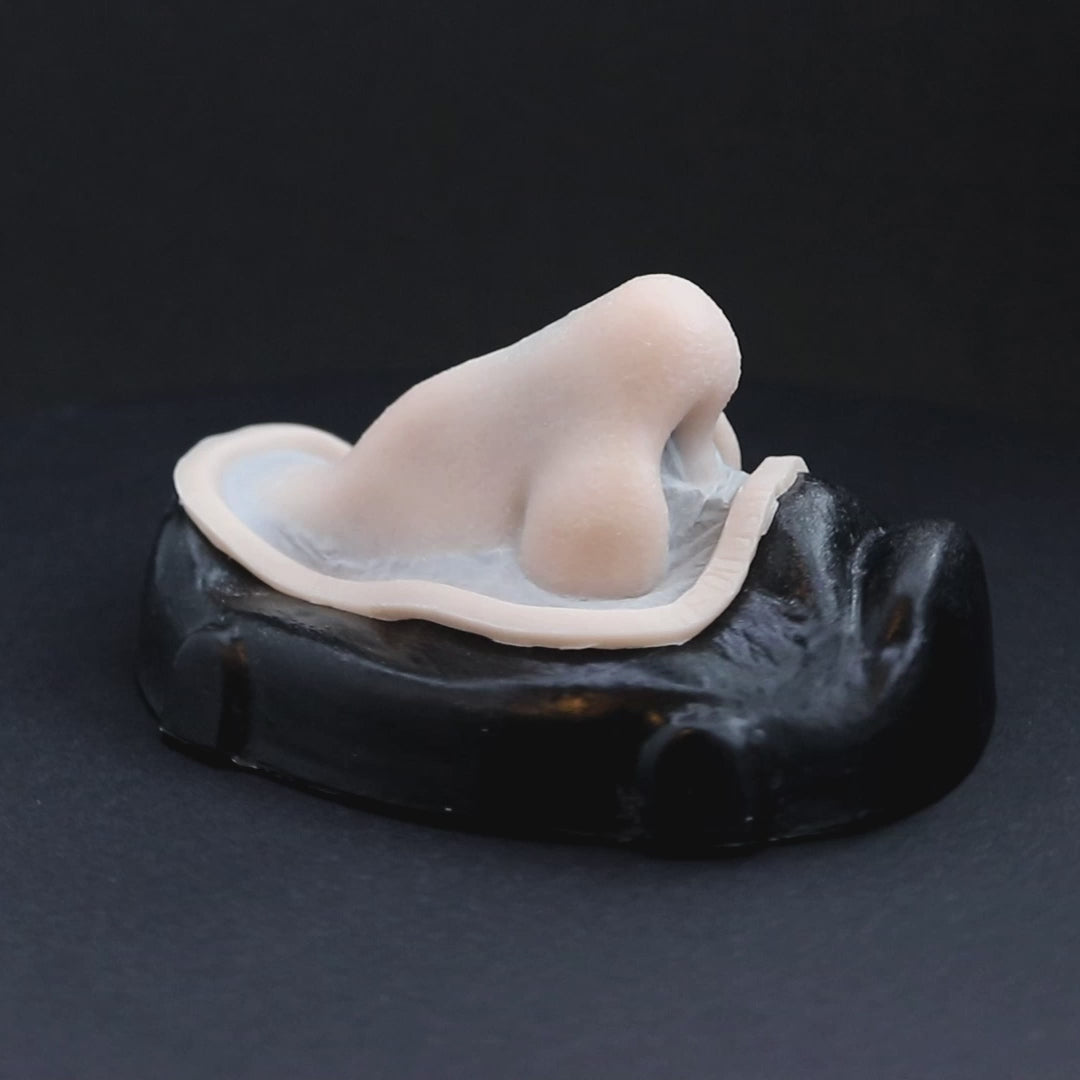 A crooked nose prosthetic in vanilla shade on a black turntable, slowly rotating.