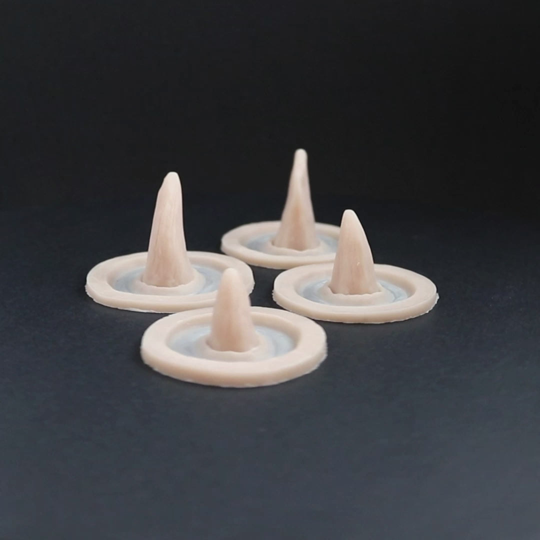Four small crooked horns prosthetics in vanilla shade on a black turntable, slowly rotating.