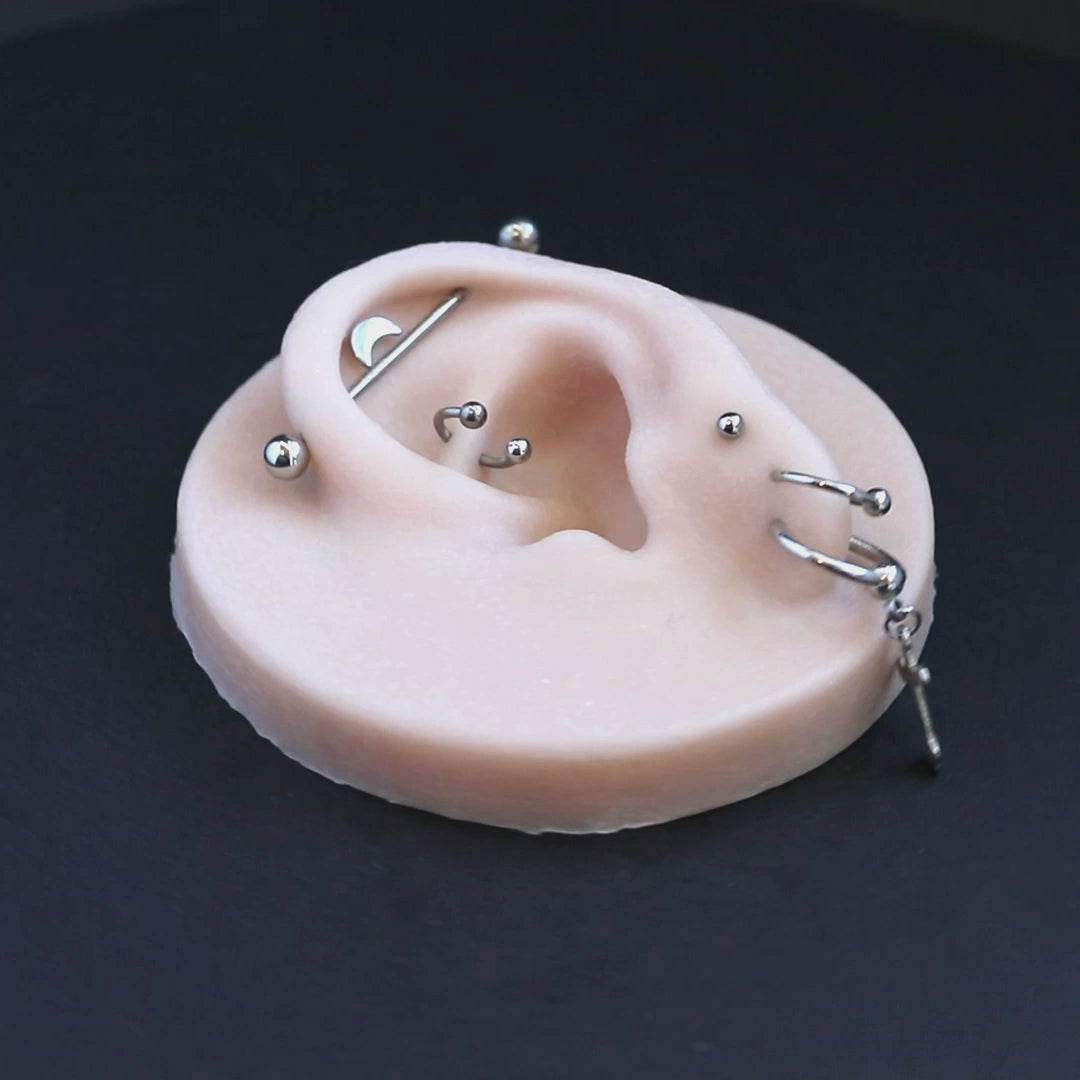 A silicone ear display piece with several earrings and piercings, on a black turntable, slowly rotating.