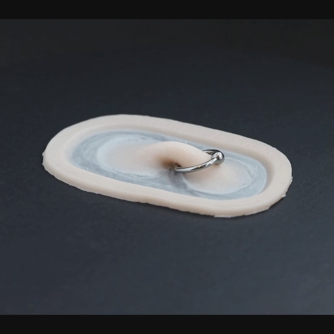 Nose bridge prosthetic, with piercing ring, in vanilla shade on a black turntable, slowly rotating.