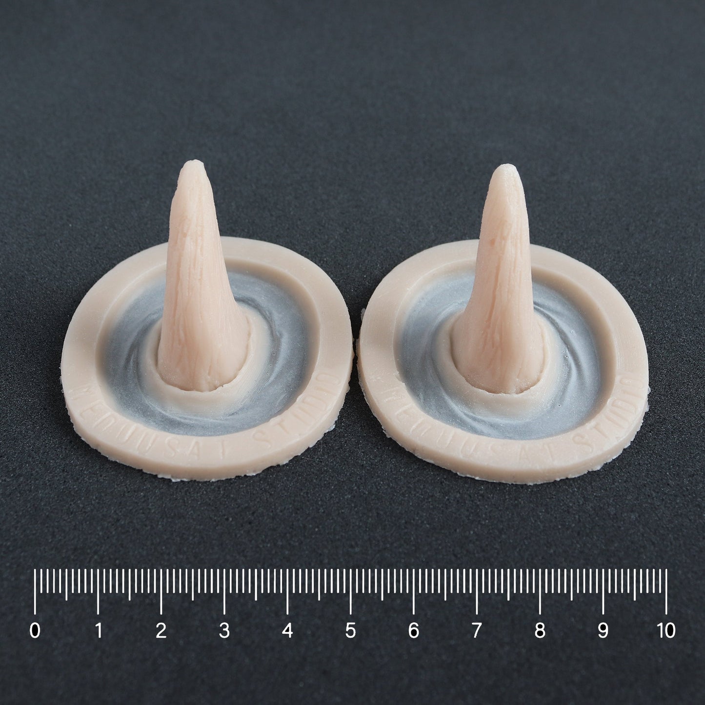 Crooked Horns (Pair) - Silicone makeup prosthetic in vanilla shade on a black surface with a ruler
