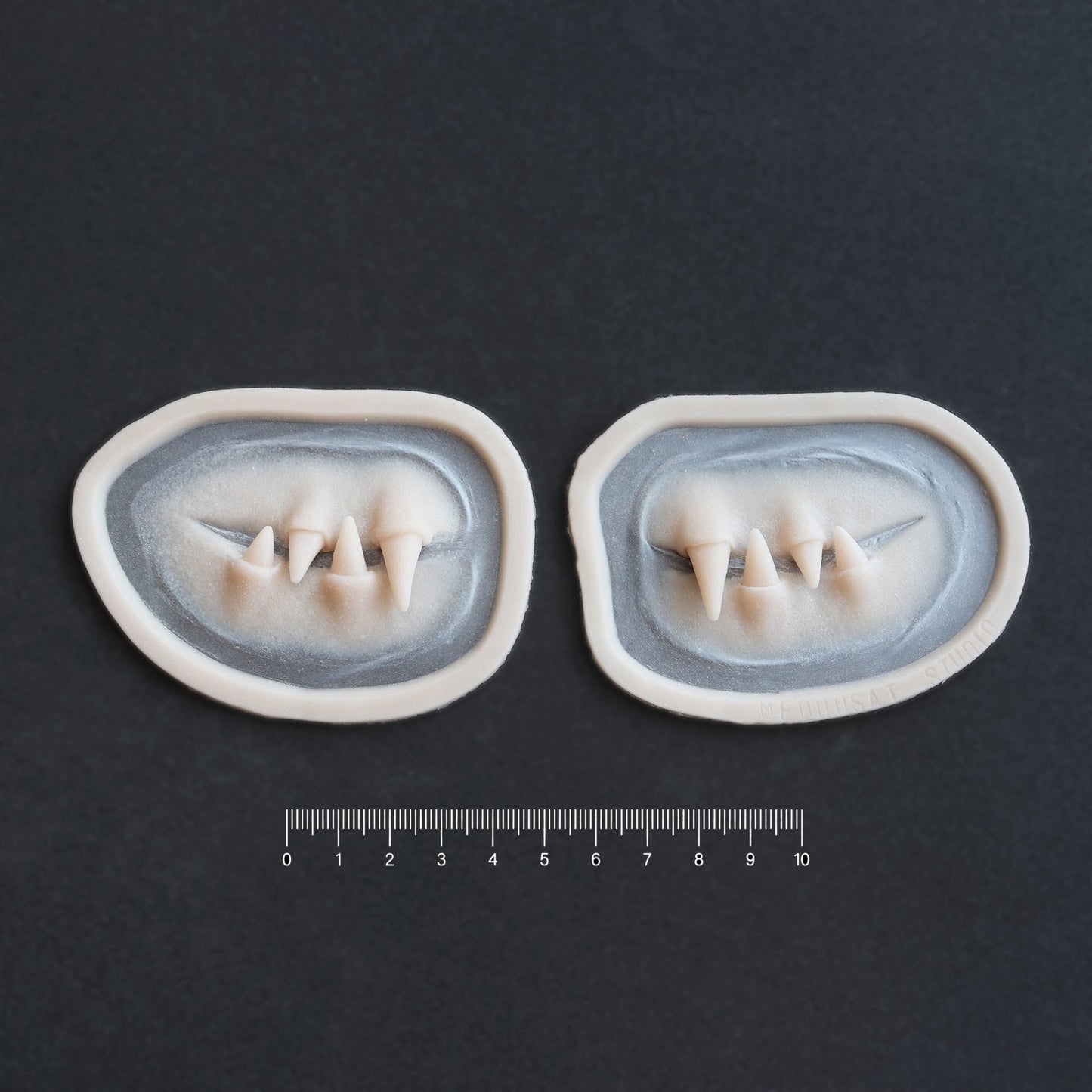 Facial Fangs 2.0 - Silicone makeup prosthetic in vanilla shade on a black surface with a ruler