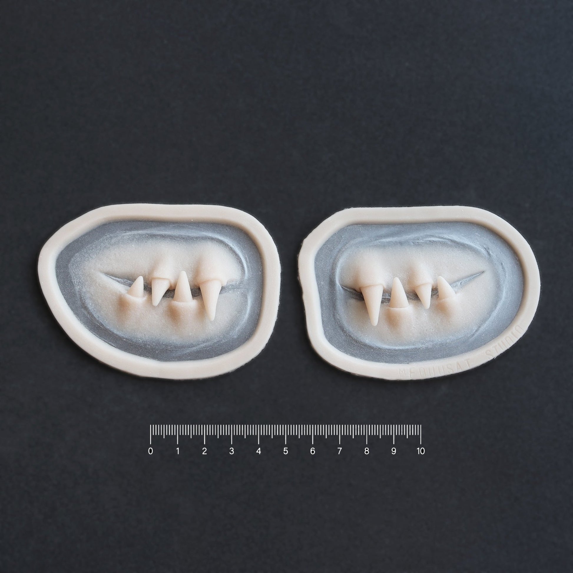 Facial Fangs 2.0 - Silicone makeup prosthetic in vanilla shade on a black surface with a ruler