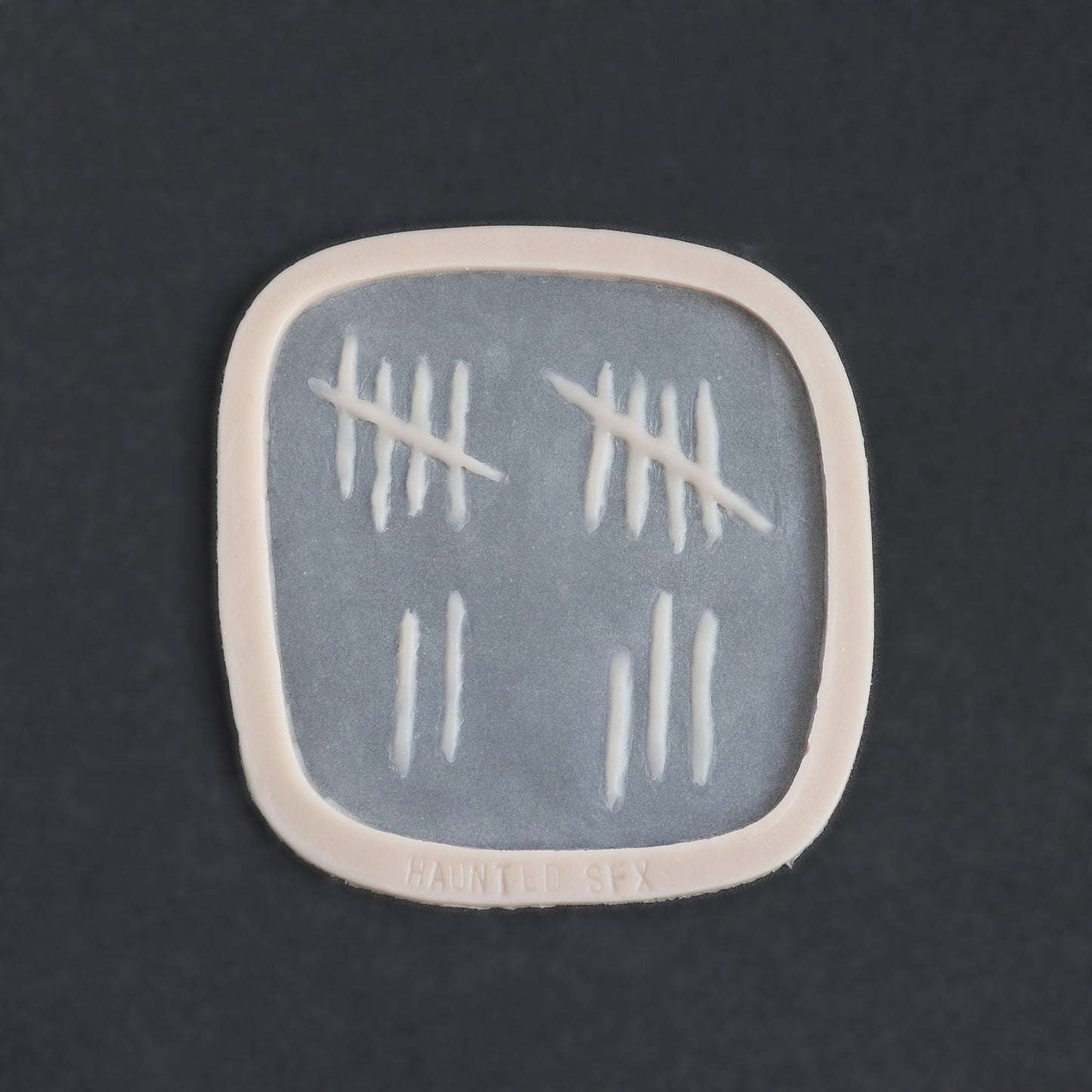 Tally Marks - Silicone makeup prosthetic in vanilla shade on a black surface