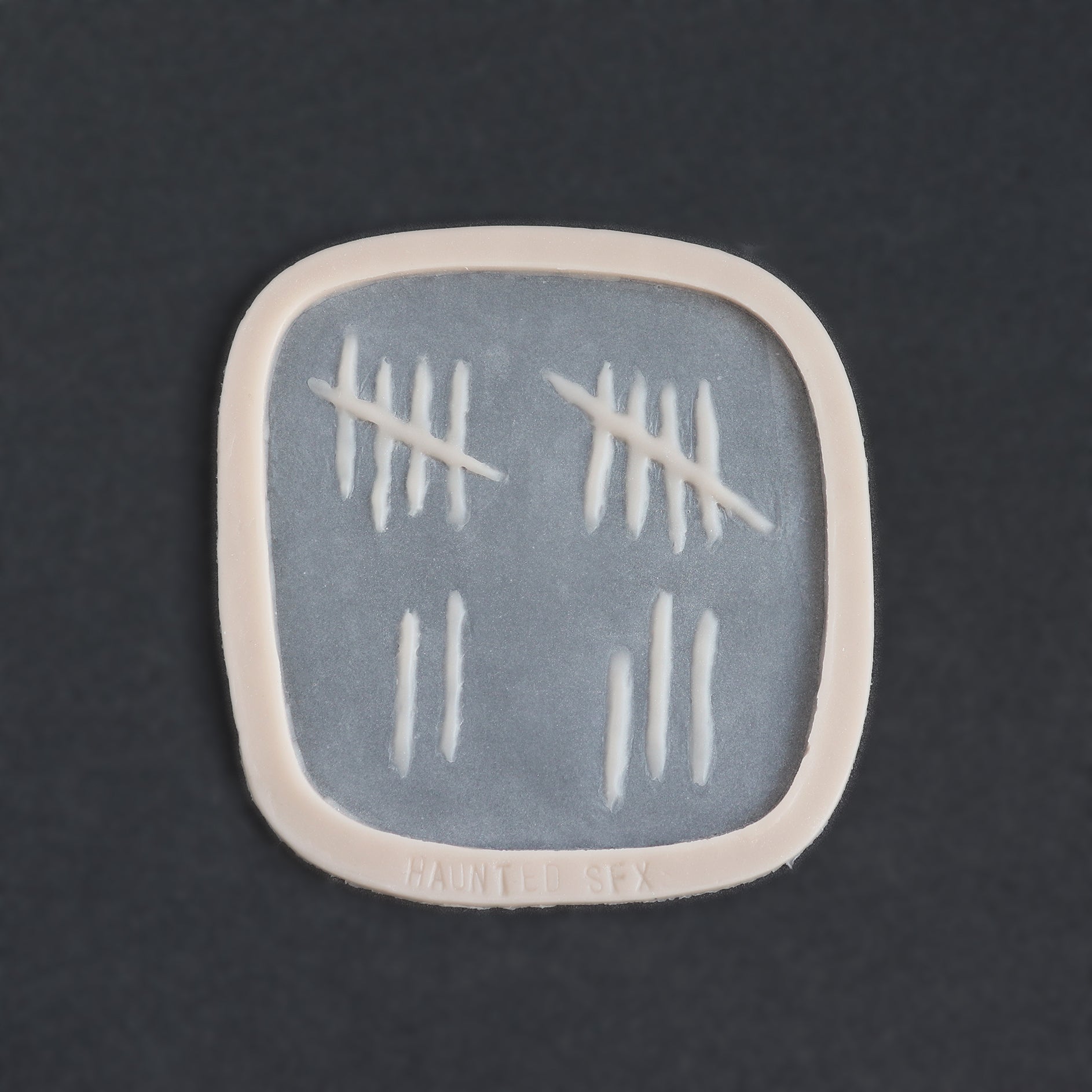 Tally Marks - Silicone makeup prosthetic in vanilla shade on a black surface