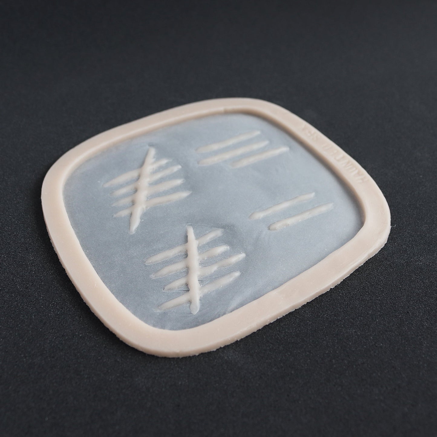 Tally Marks - Silicone makeup prosthetic in vanilla shade on a black surface