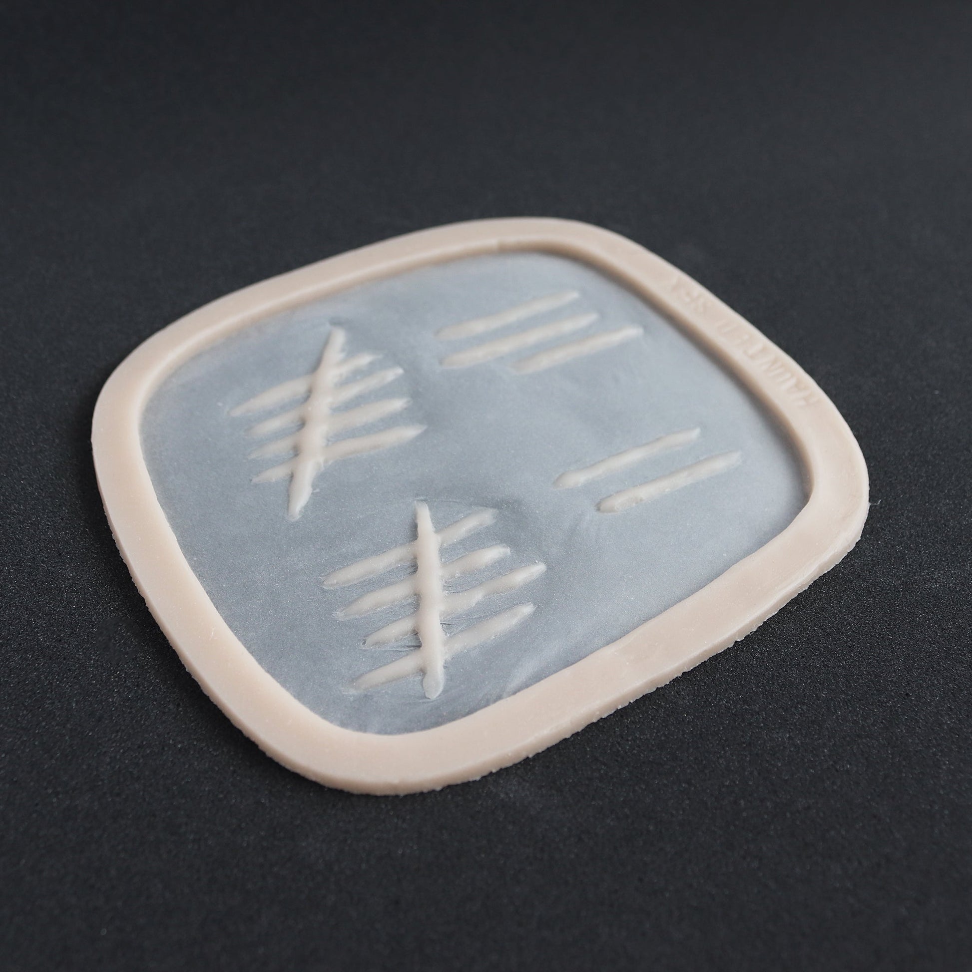 Tally Marks - Silicone makeup prosthetic in vanilla shade on a black surface