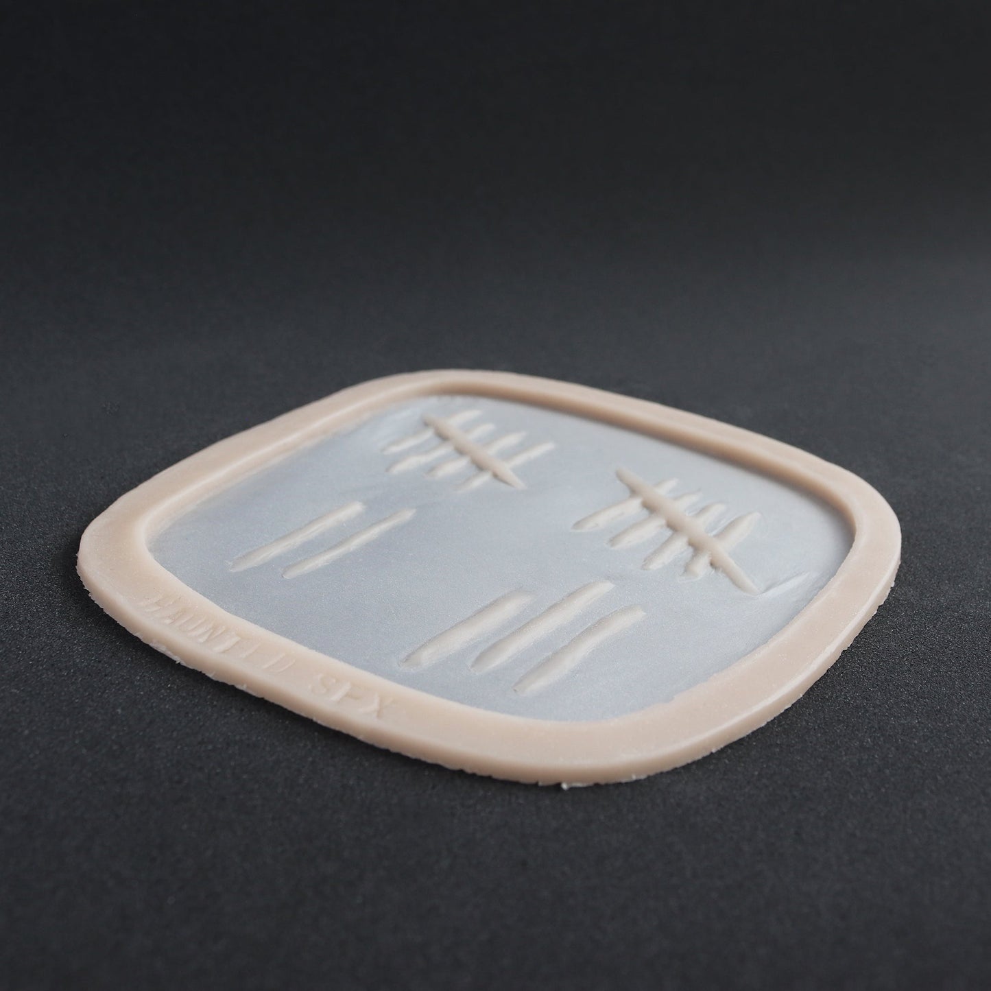 Tally Marks - Silicone makeup prosthetic in vanilla shade on a black surface