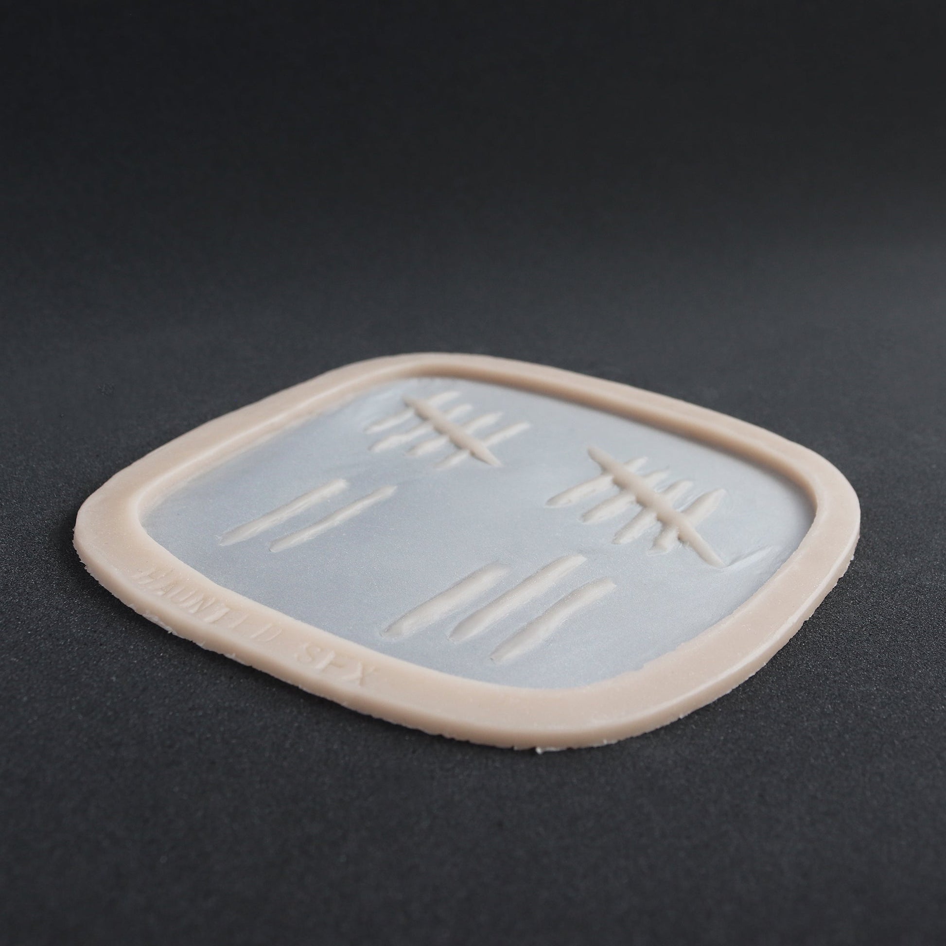Tally Marks - Silicone makeup prosthetic in vanilla shade on a black surface