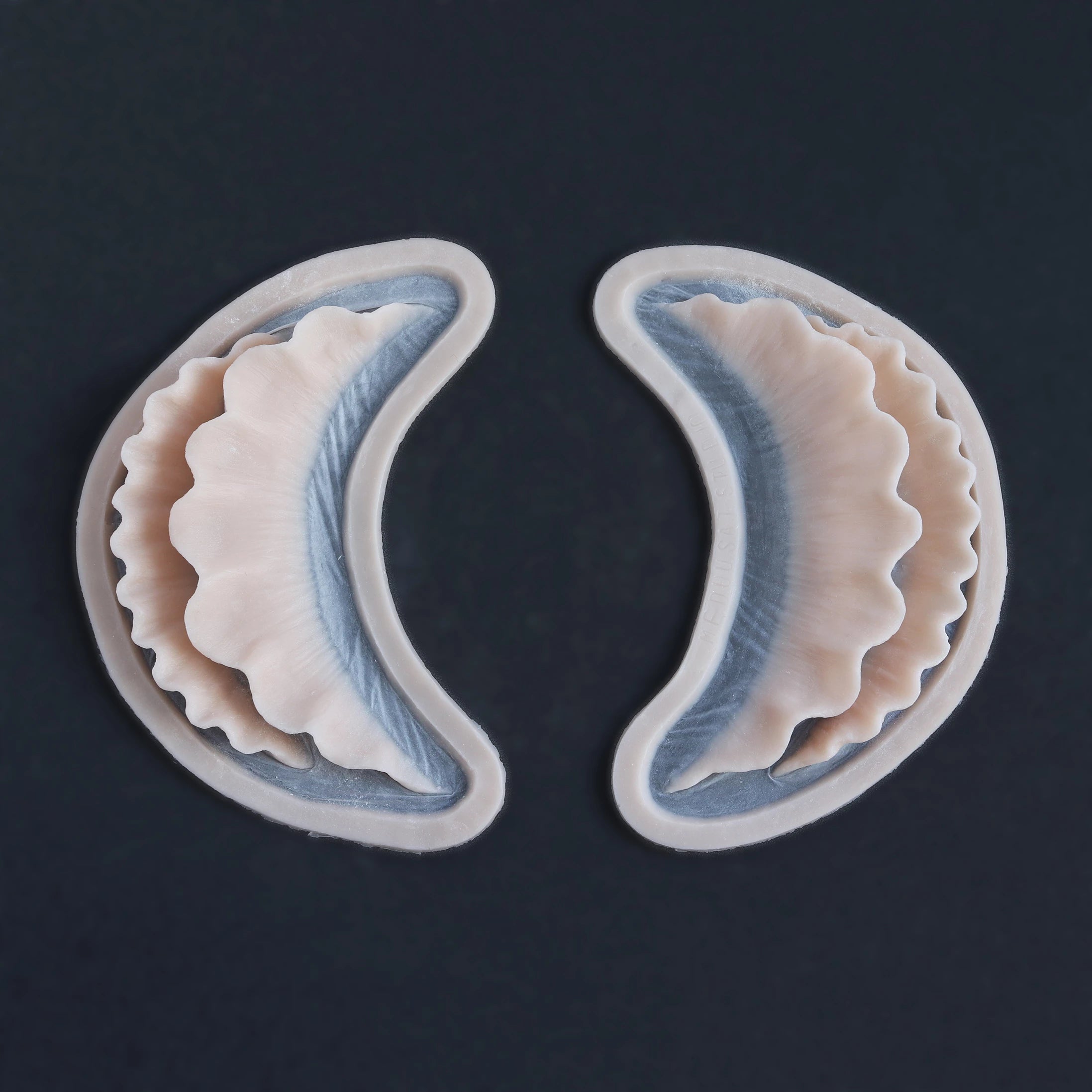 Pair of ruffle gills silicone prosthetics in vanilla shade on a black surface