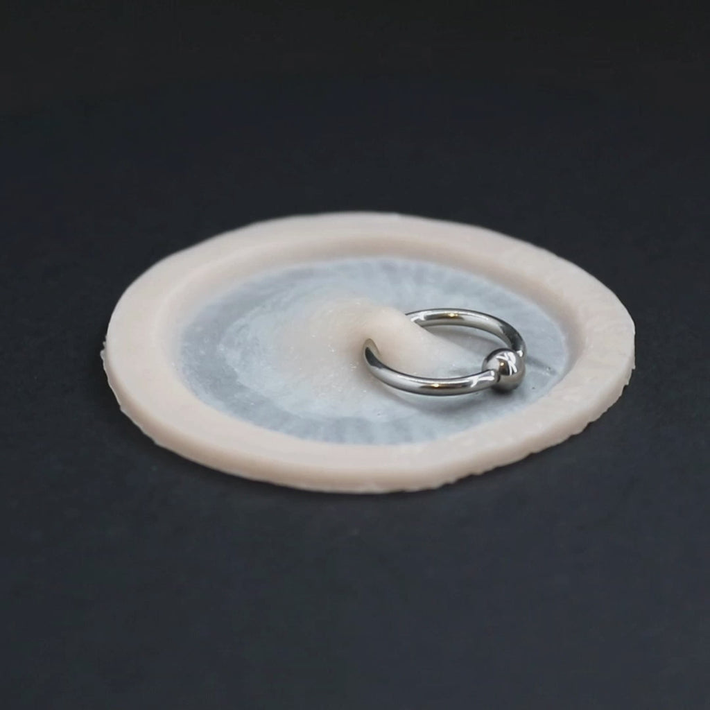 Surface piercing, with ring, prosthetic in vanilla shade on a black turntable, slowly rotating. 