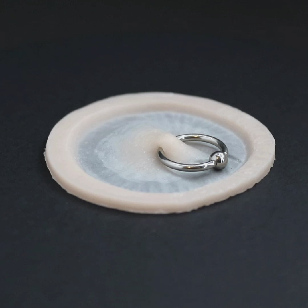 Surface piercing, with ring, prosthetic in vanilla shade on a black turntable, slowly rotating. 