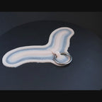 Subdermal choker, with steel ring, prosthetic in vanilla shade on a black turntable, slowly rotating. 