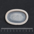 666 Carving prosthetic in vanilla shade on a black surface with a ruler