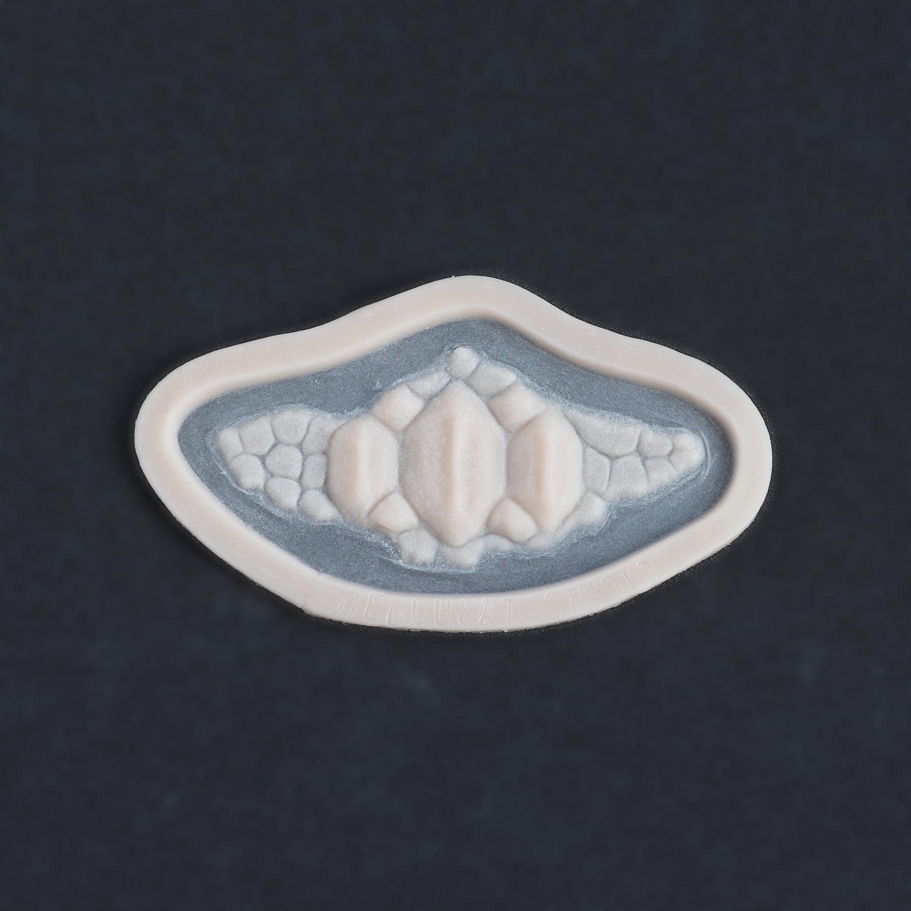 Alligator Scales chin piece in vanilla shade on a black surface.