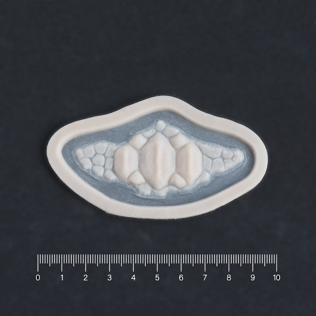 Alligator Scales chin piece in vanilla shade on a black surface with a ruler.