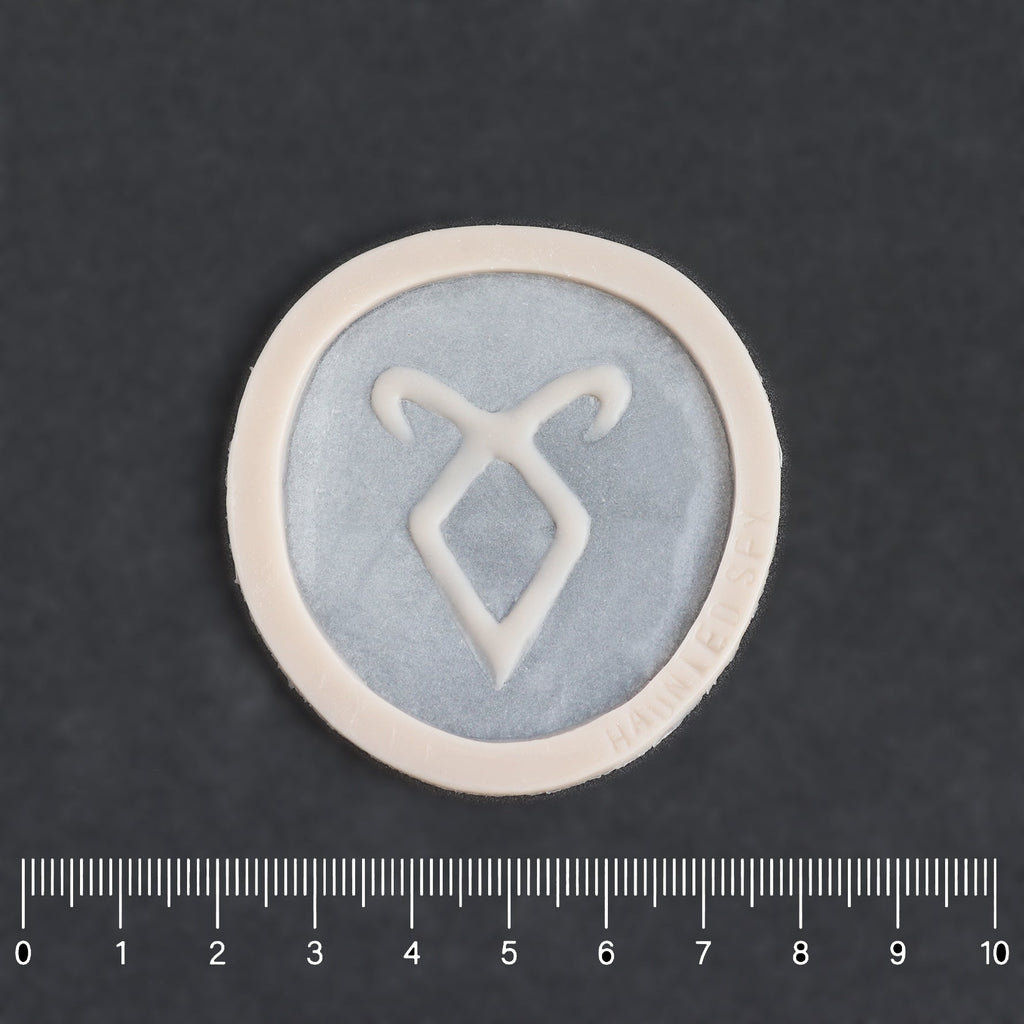 Angel Rune Scarification in vanilla shade on a black surface with a ruler.