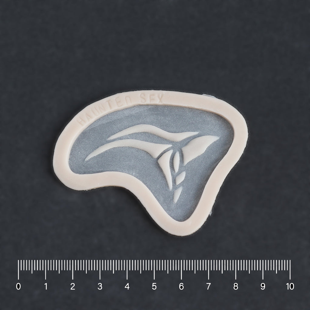 Anubis Mark - Silicone makeup prosthetic in vanilla shade on a black surface with a ruler