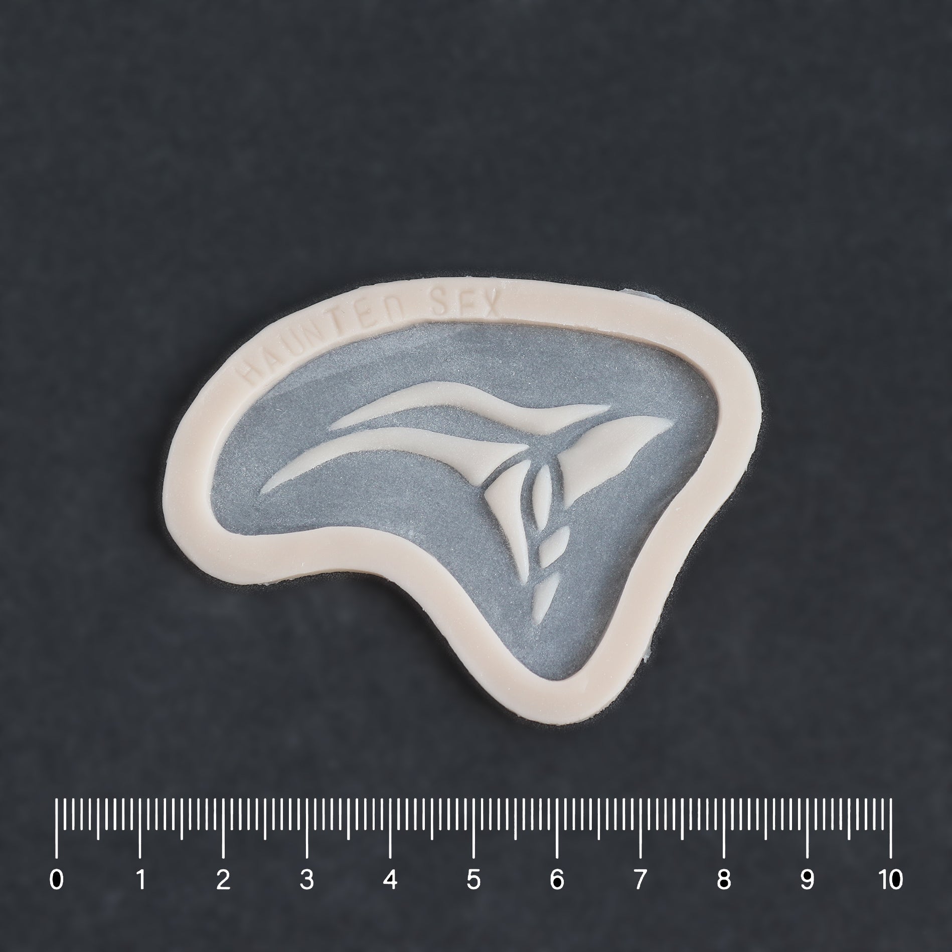 Anubis Mark - Silicone makeup prosthetic in vanilla shade on a black surface with a ruler