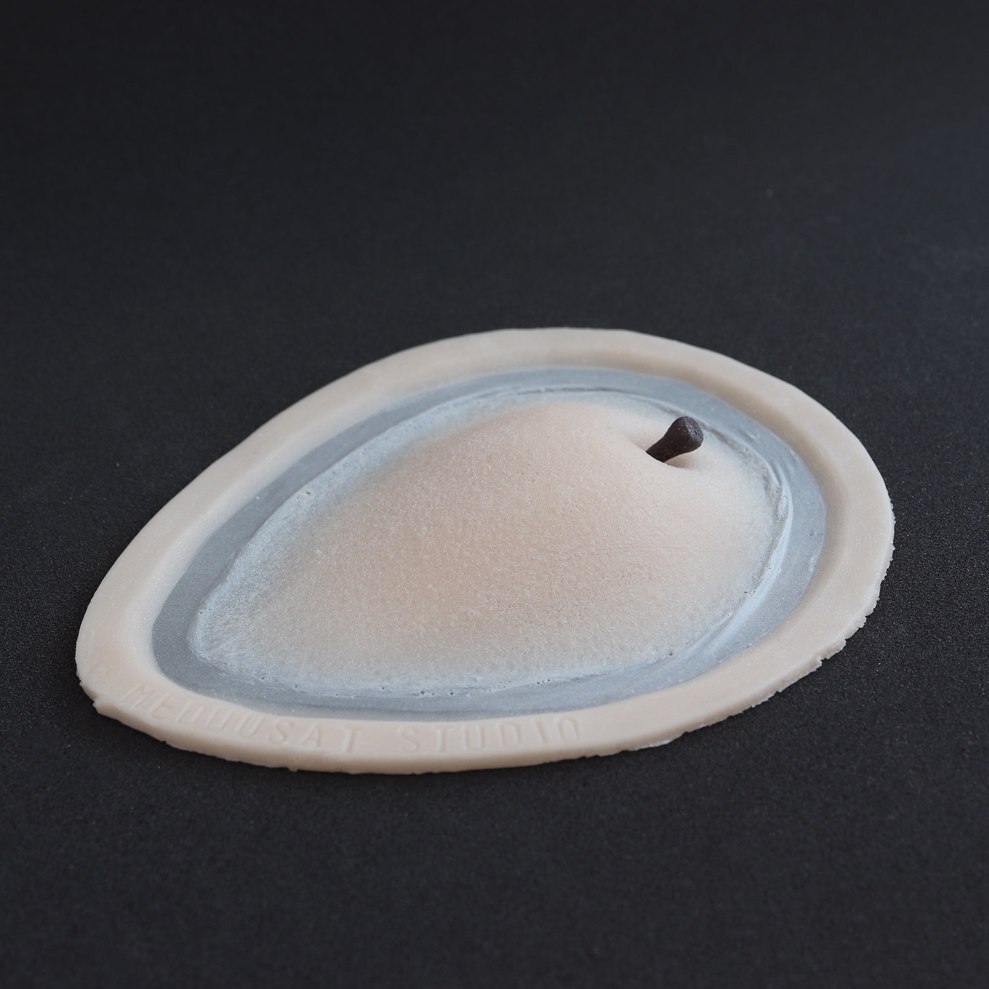 Apple Cheek prosthetic in vanilla shade on a black surface at an angle.