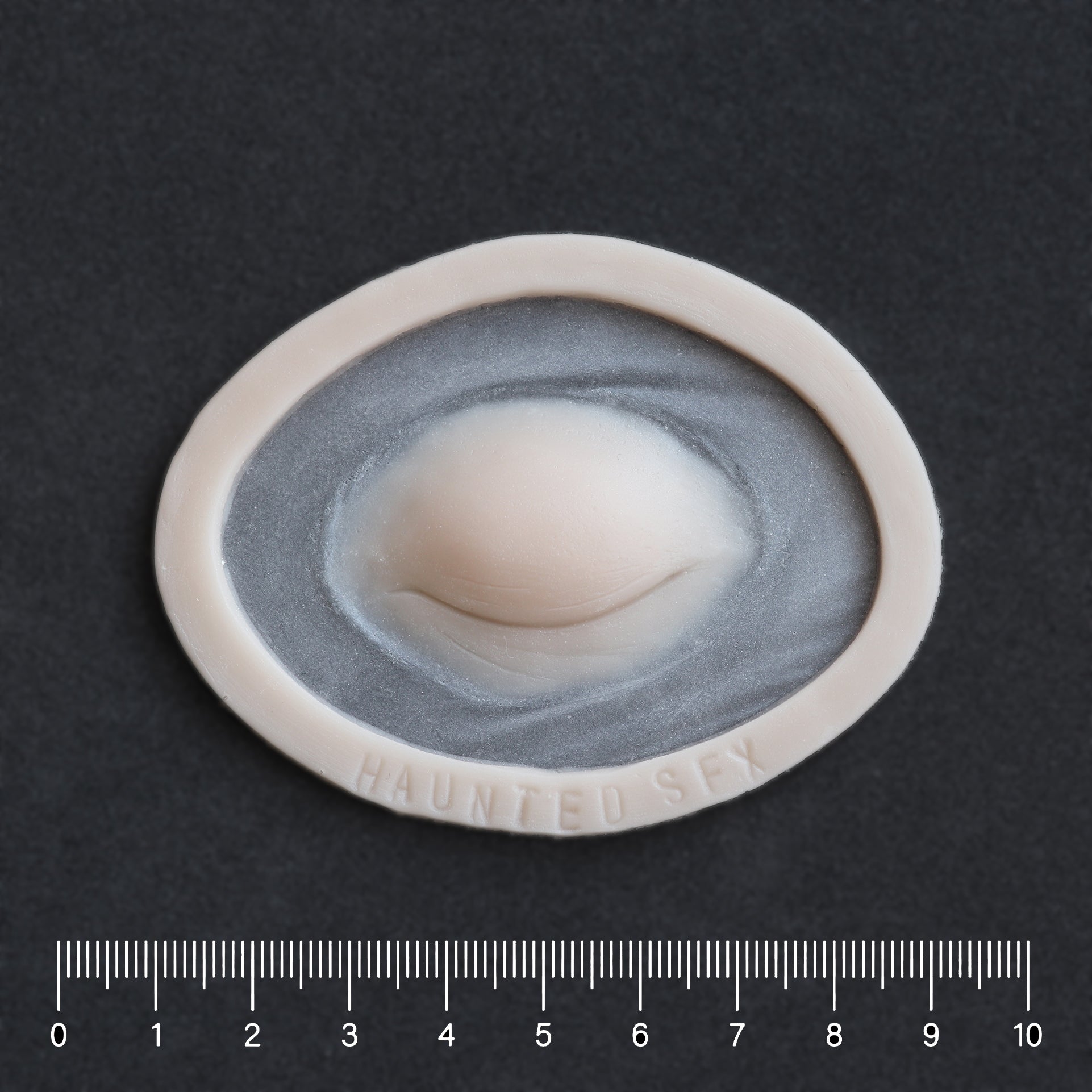 Closed Third Eye - Silicone makeup prosthetic in vanilla shade on a black surface with a ruler