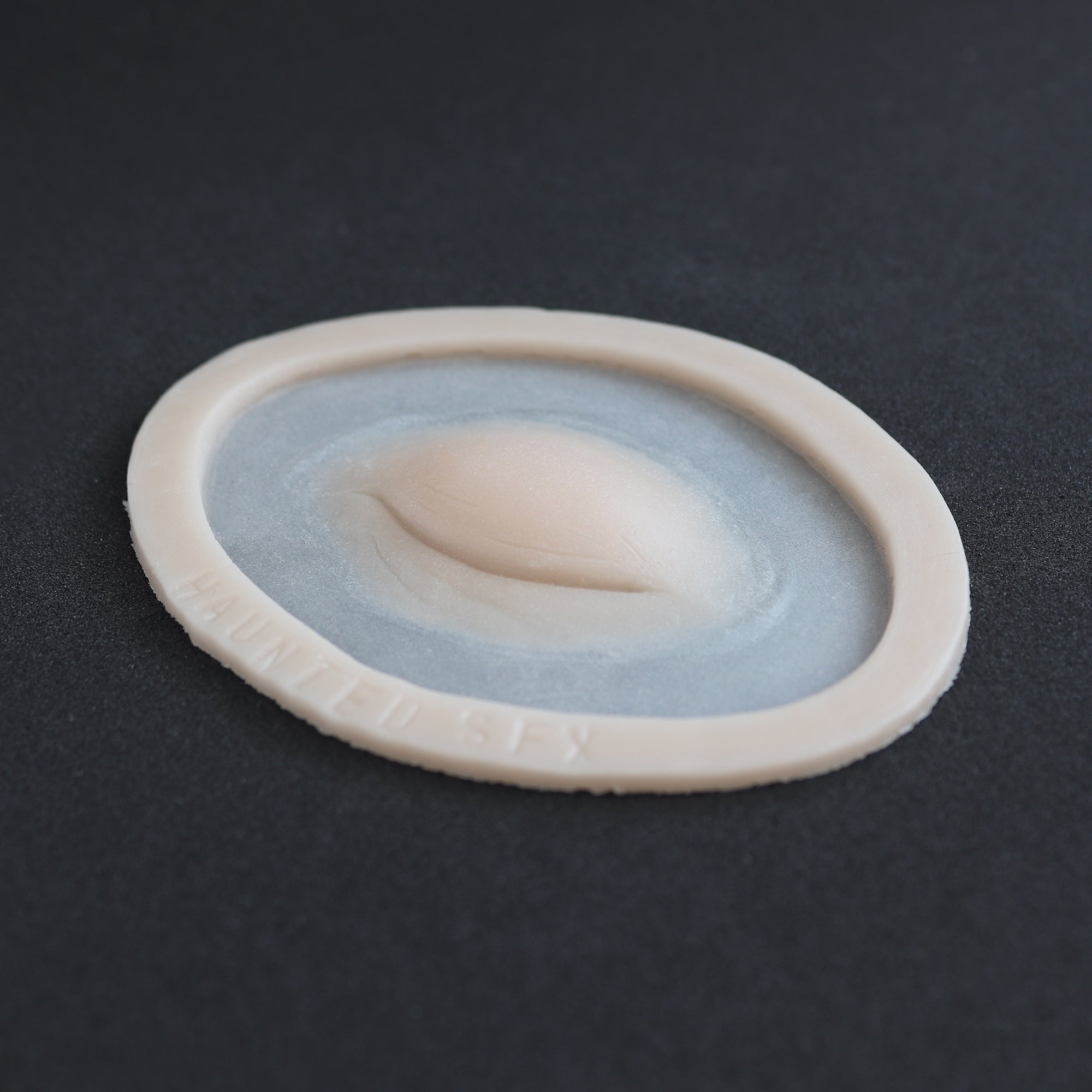 Closed Third Eye - Silicone makeup prosthetic in vanilla shade on a black surface at an angle