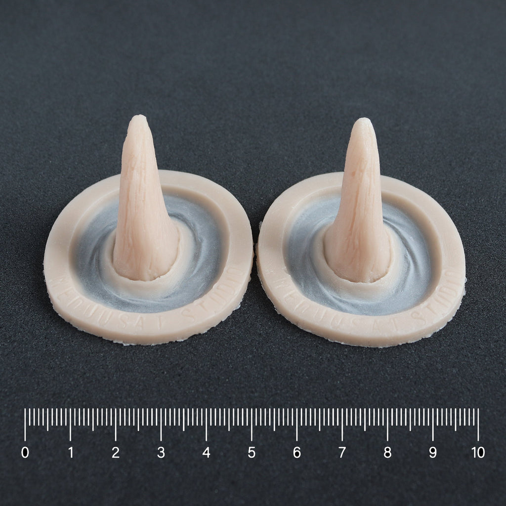 Crooked Horns (Pair) - Silicone makeup prosthetic in vanilla shade on a black surface with a ruler