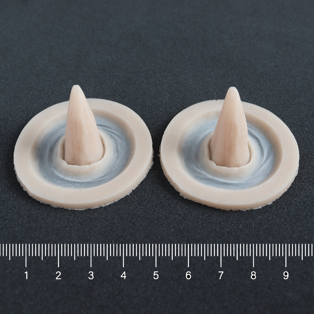 Crooked Horns (Pair) - Silicone makeup prosthetic in vanilla shade on a black surface with a ruler