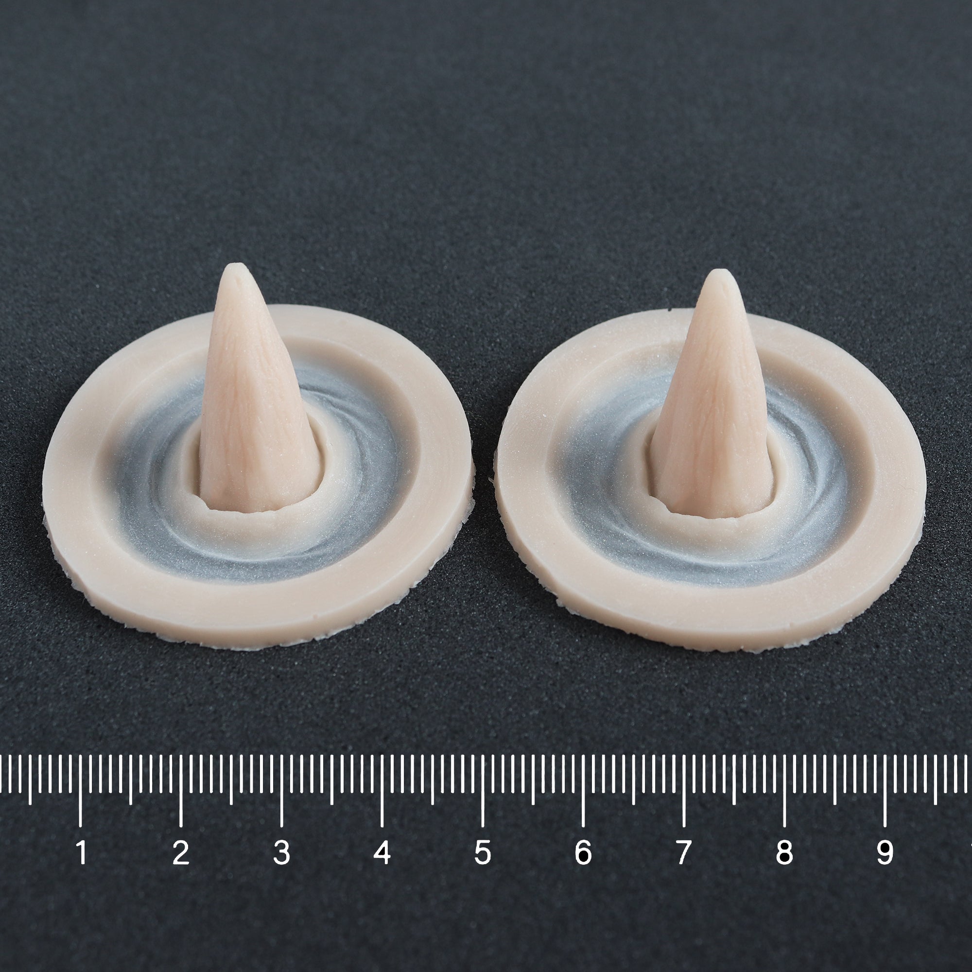 Crooked Horns (Pair) - Silicone makeup prosthetic in vanilla shade on a black surface with a ruler