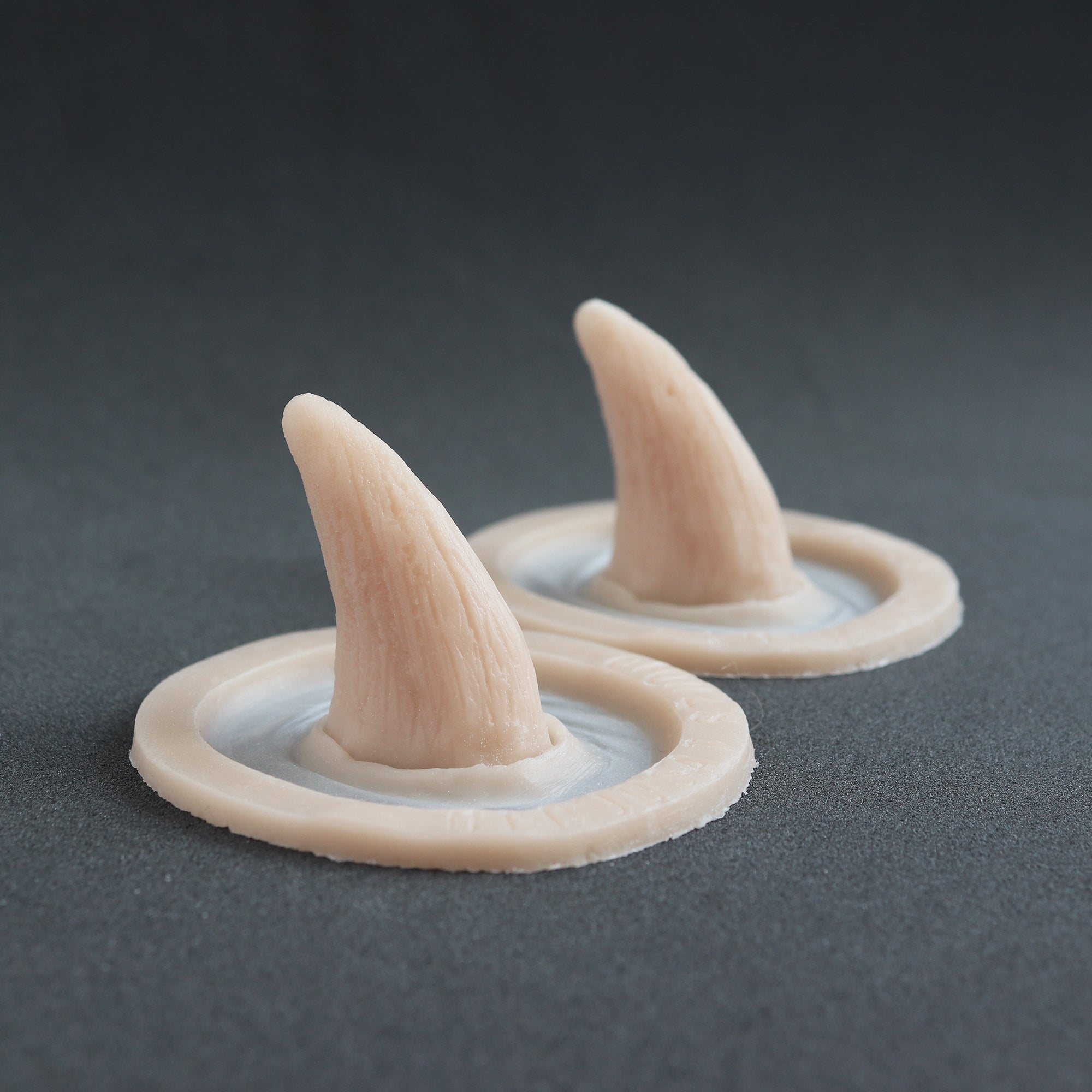 Crooked Horns (Pair) - Silicone makeup prosthetic in vanilla shade on a black surface