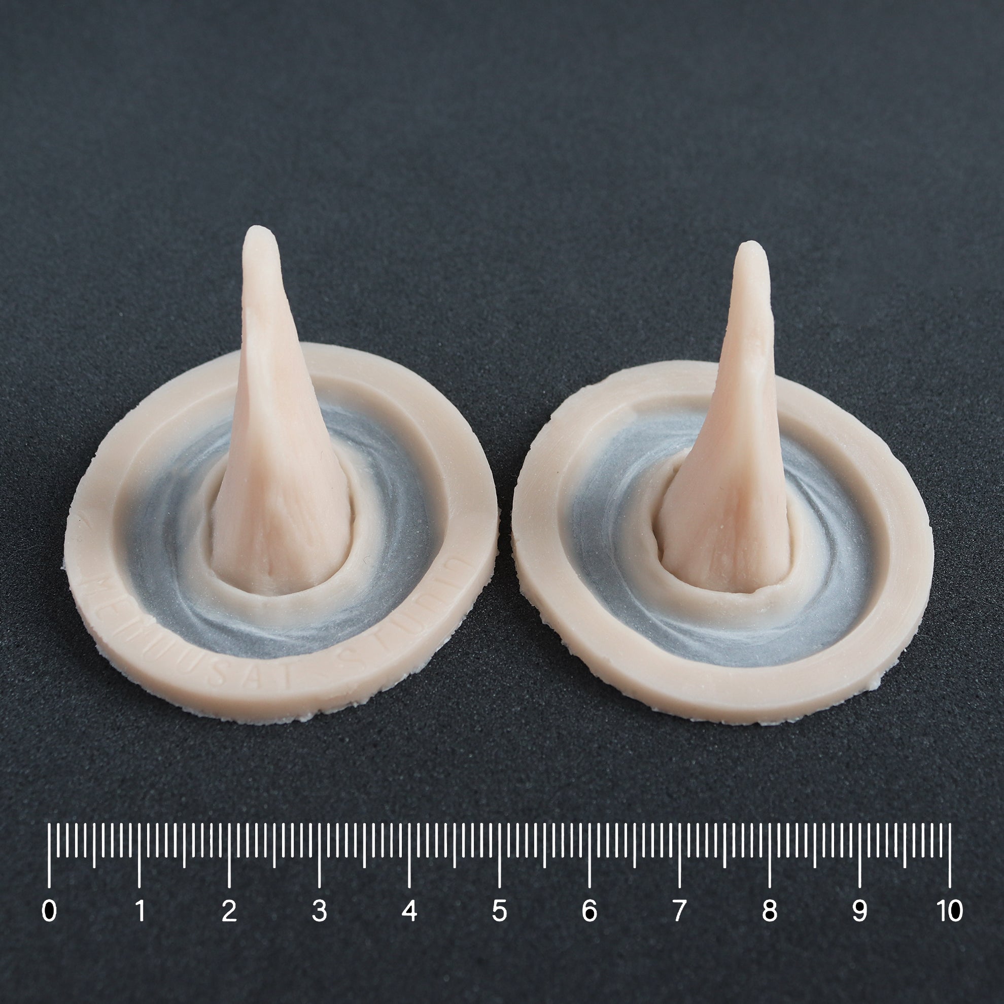 Crooked Horns (Pair) - Silicone makeup prosthetic in vanilla shade on a black surface with a ruler