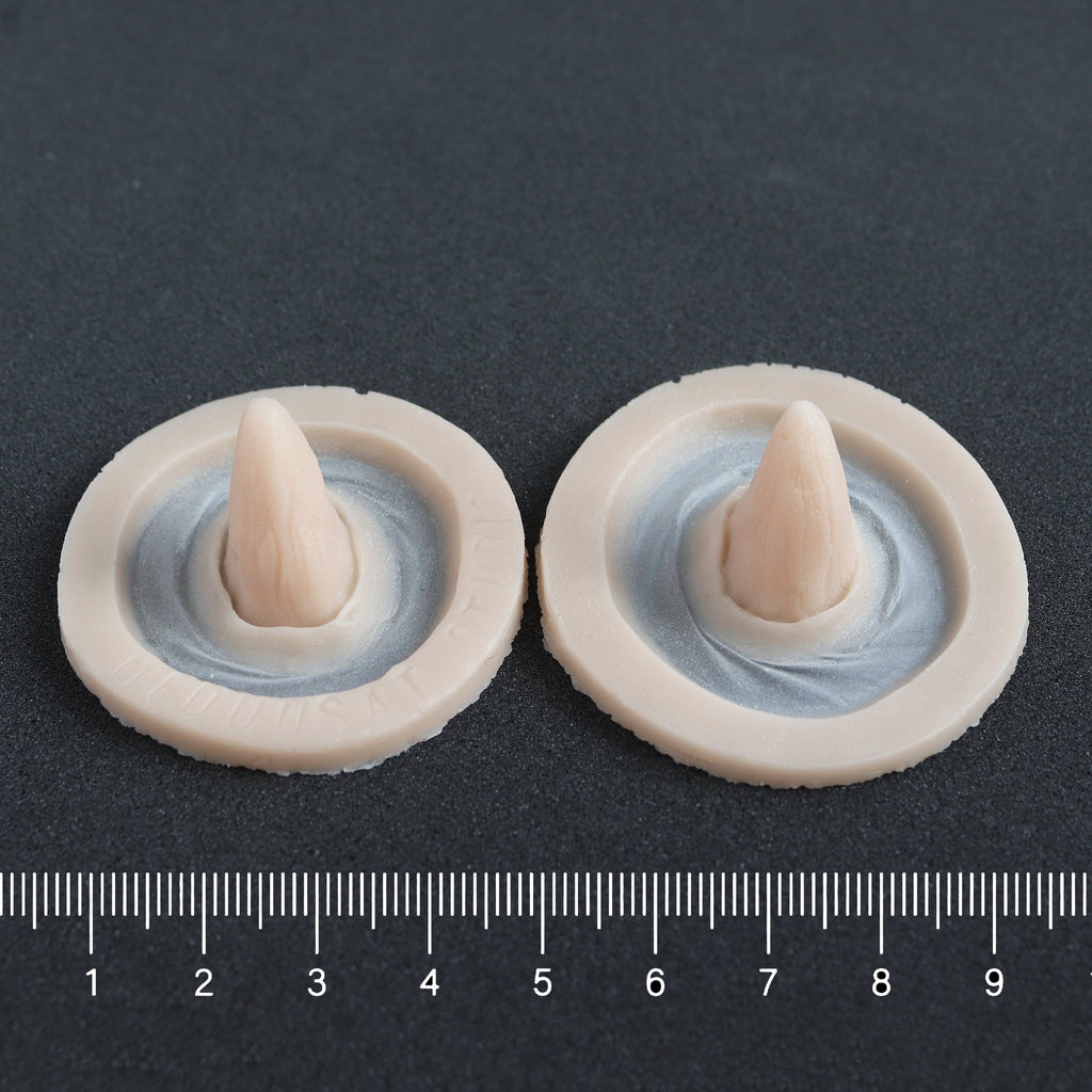Crooked Horns (Pair) - Silicone makeup prosthetic in vanilla shade on a black surface with a ruler