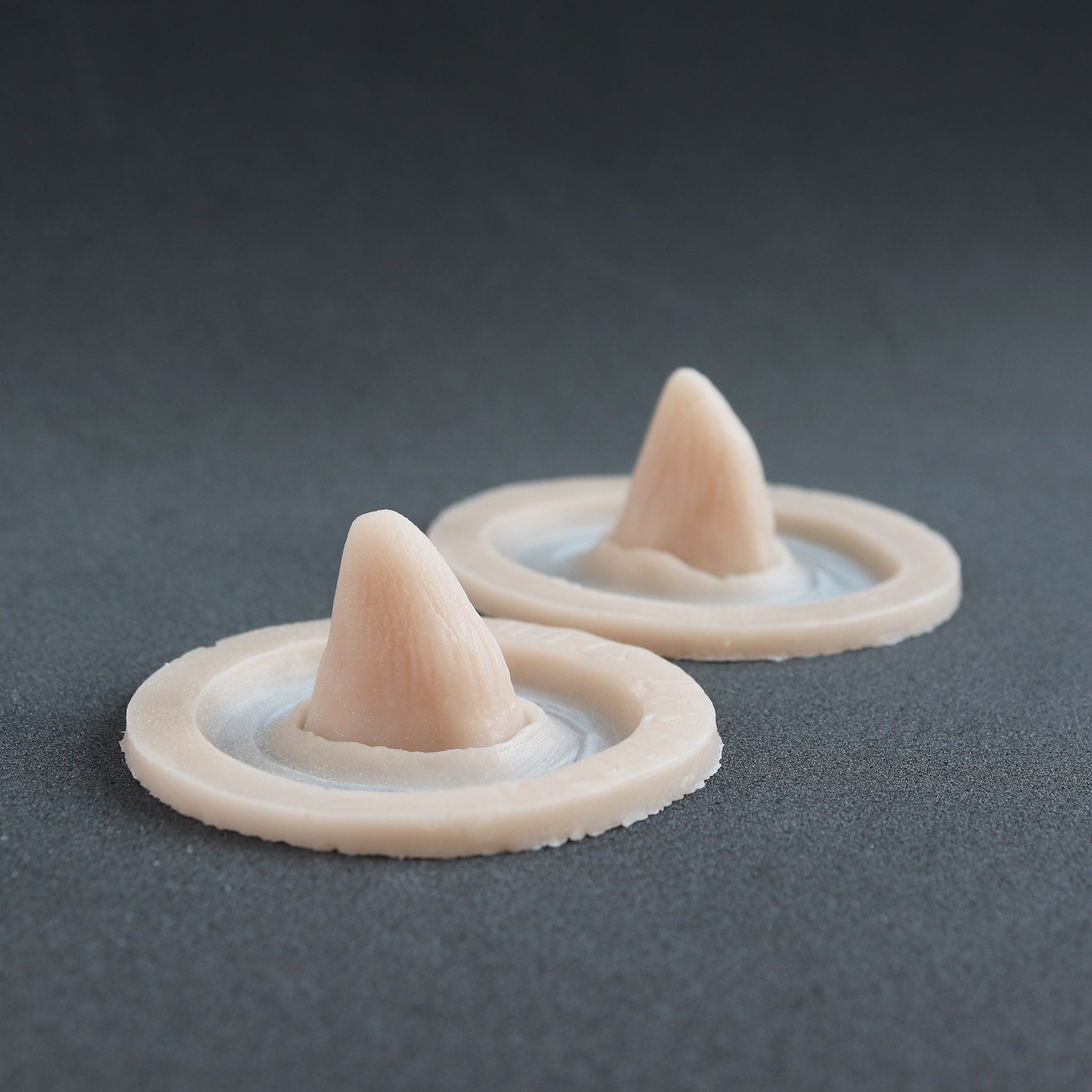 Crooked Horns (Pair) - Silicone makeup prosthetic in vanilla shade on a black surface