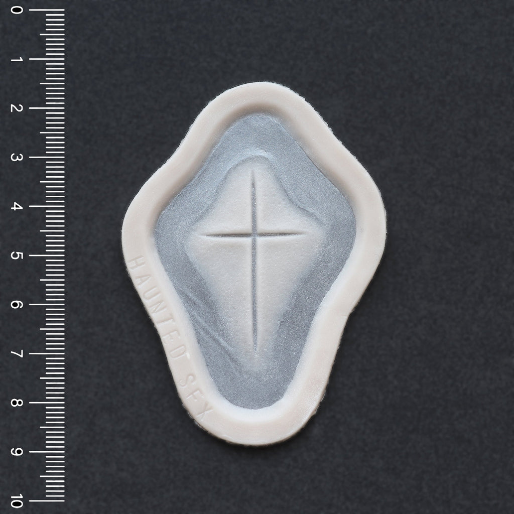 Cross Carving - Silicone makeup prosthetic in vanilla shade on a black surface with a ruler