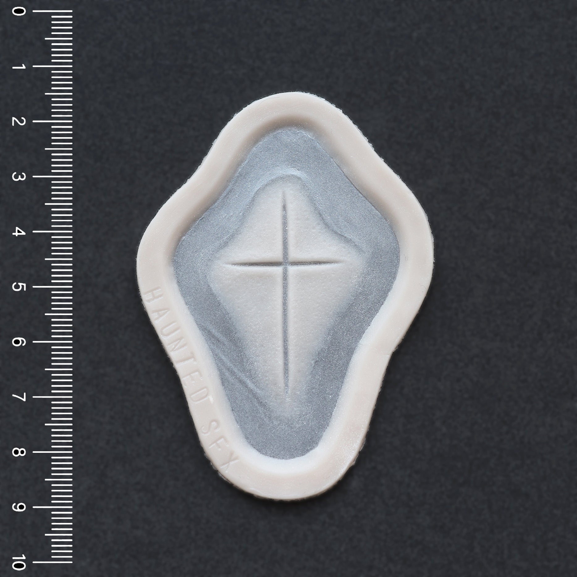 Cross Carving - Silicone makeup prosthetic in vanilla shade on a black surface with a ruler