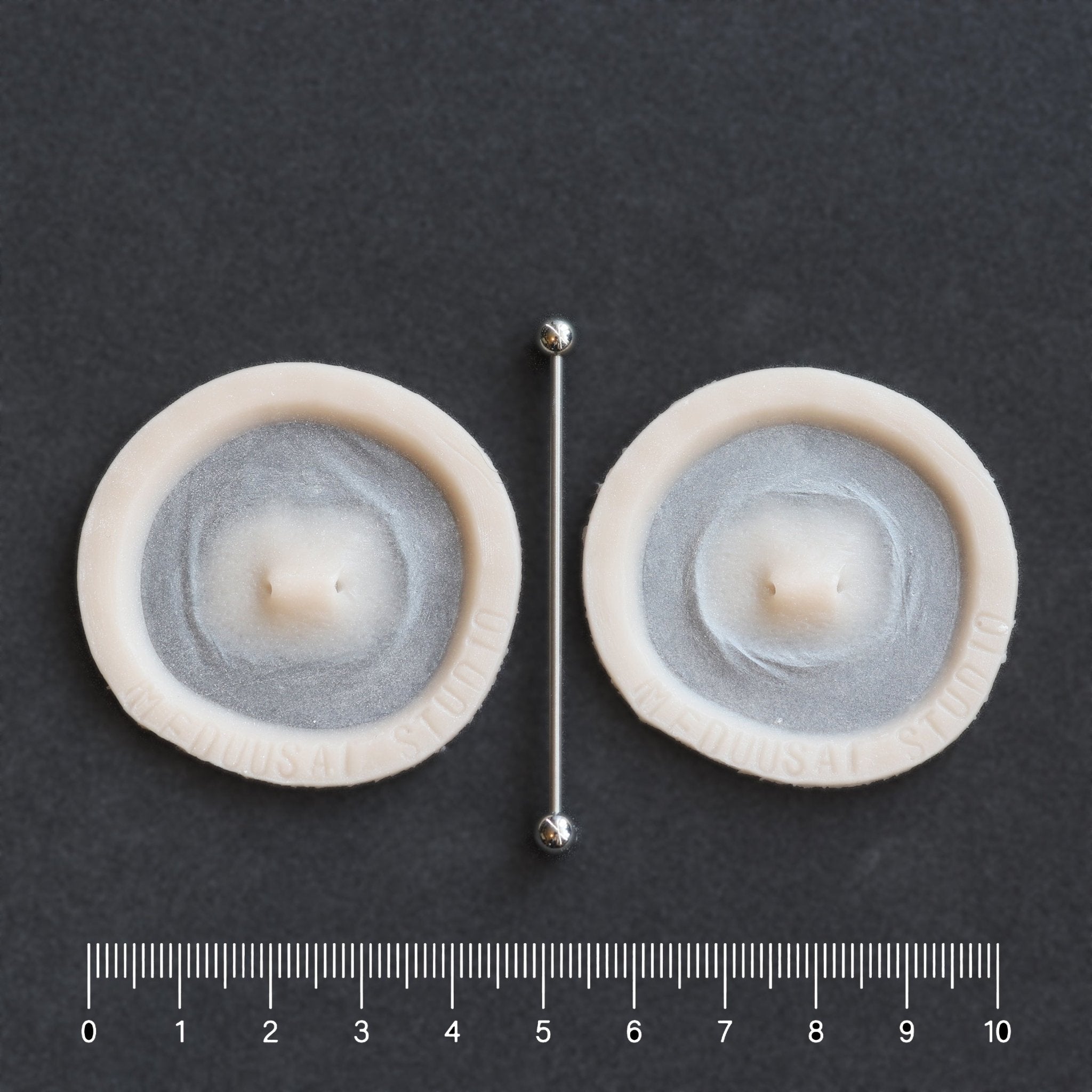 Double Surface Piercing - Silicone makeup prosthetic in vanilla shade on a black surface with a ruler