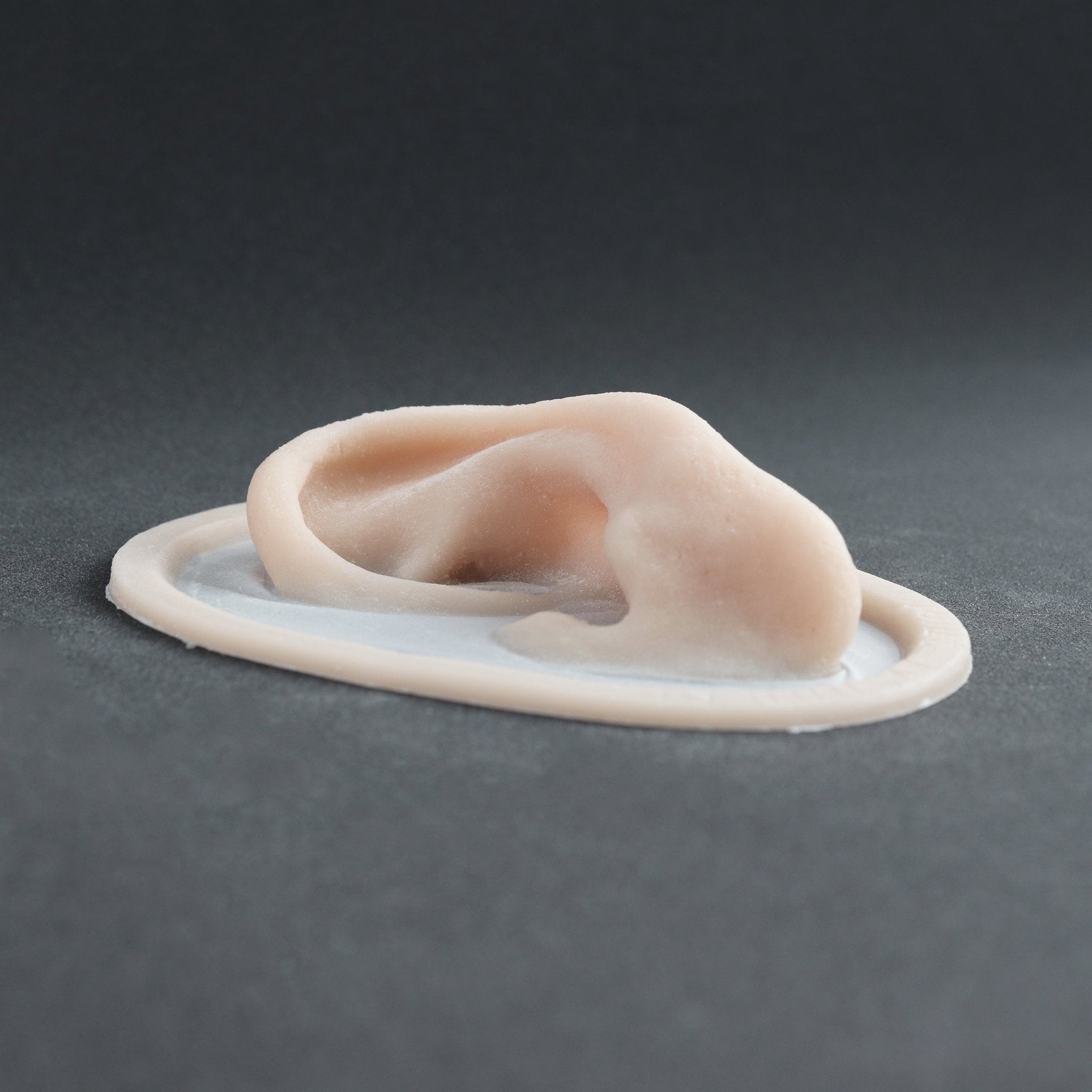 Extra Ears - Silicone makeup prosthetic in vanilla shade on a black surface