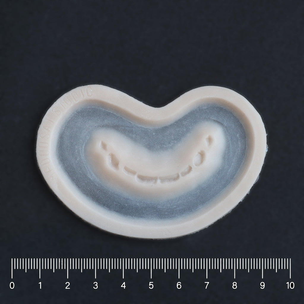 Half Bite - Silicone makeup prosthetic in vanilla shade on a black surface with a ruler