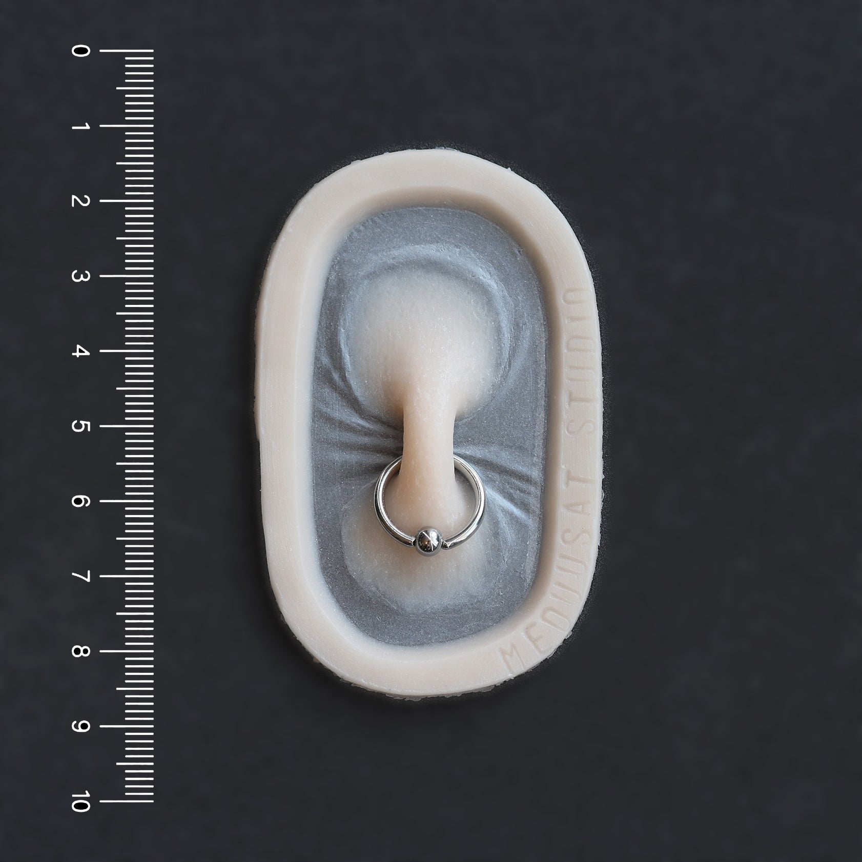 Nose Bridge - Silicone makeup prosthetic in vanilla shade on a black surface with a ruler