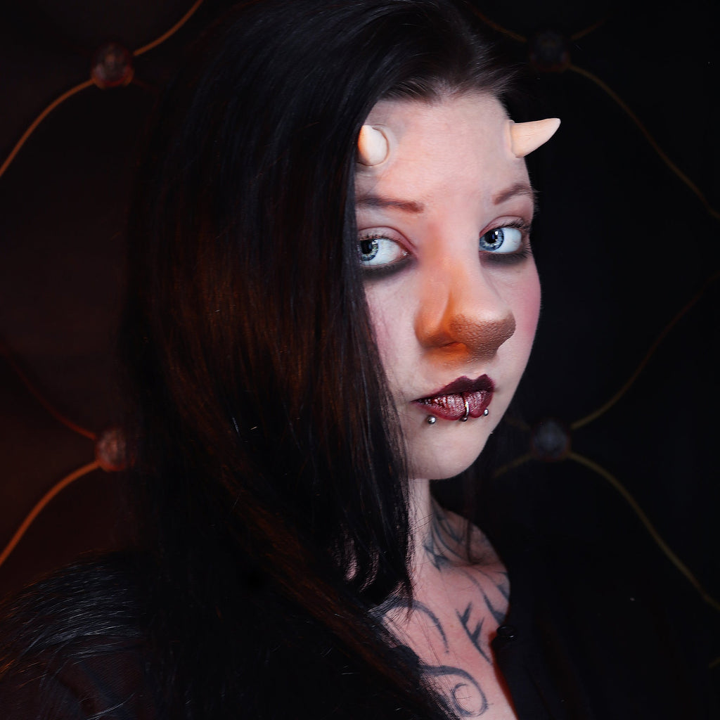 Woman with black hair wearing crooked horns and a satyr nose prosthetic