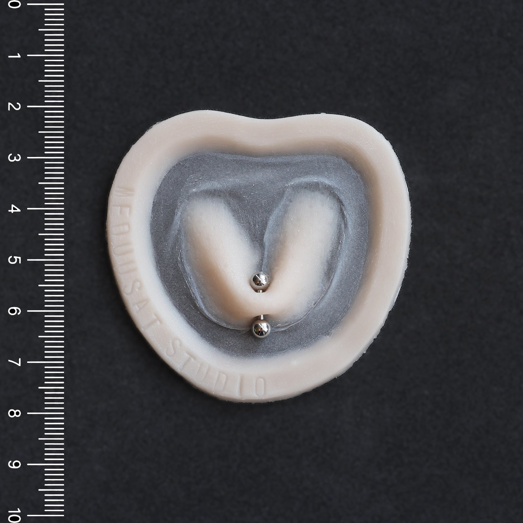 Stretched Piercing - Silicone makeup prosthetic in vanilla shade on a black surface with a ruler