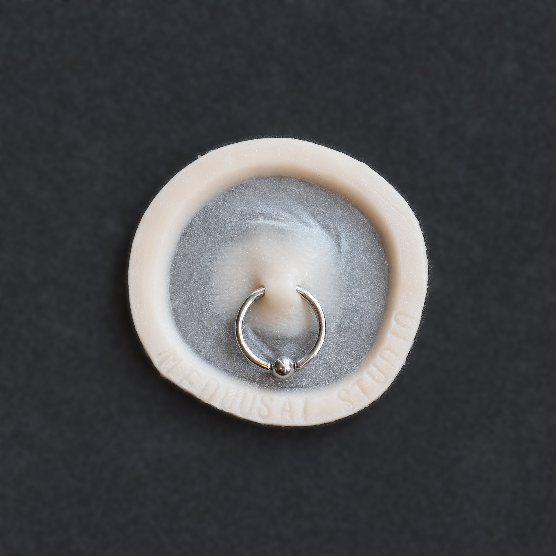 Surface Piercing - Silicone makeup prosthetic in vanilla shade on a black surface