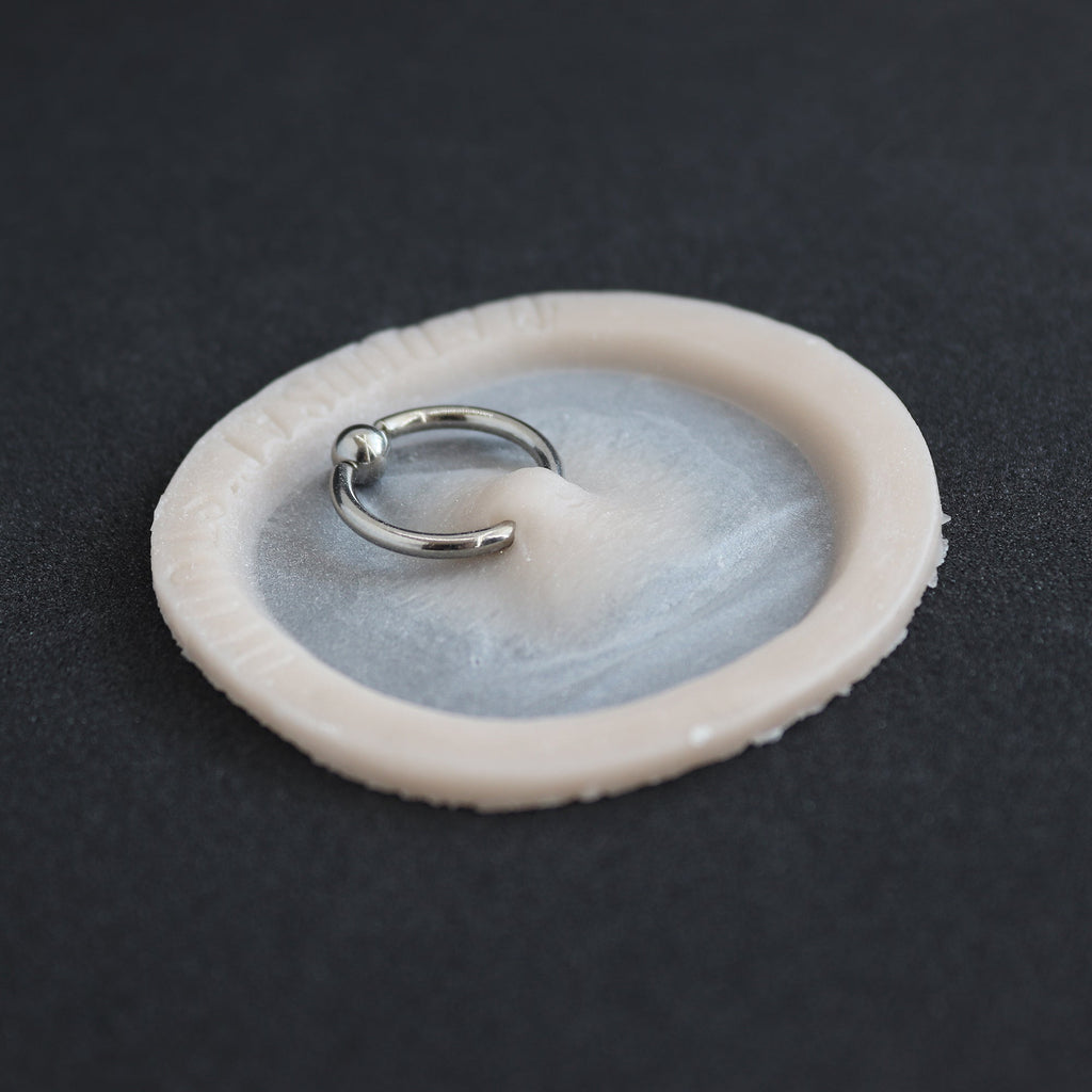 Surface Piercing - Silicone makeup prosthetic in vanilla shade on a black surface