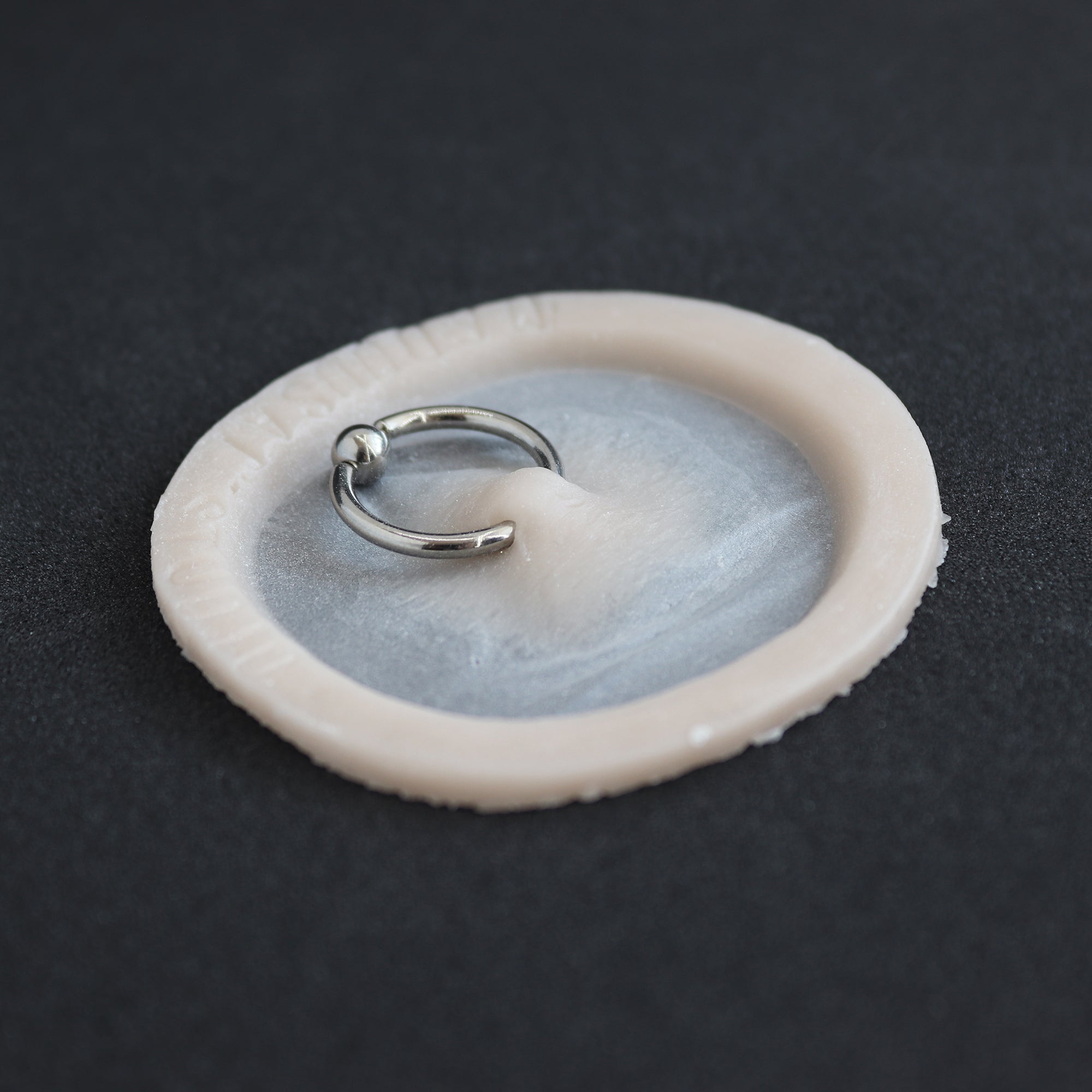 Surface Piercing - Silicone makeup prosthetic in vanilla shade on a black surface