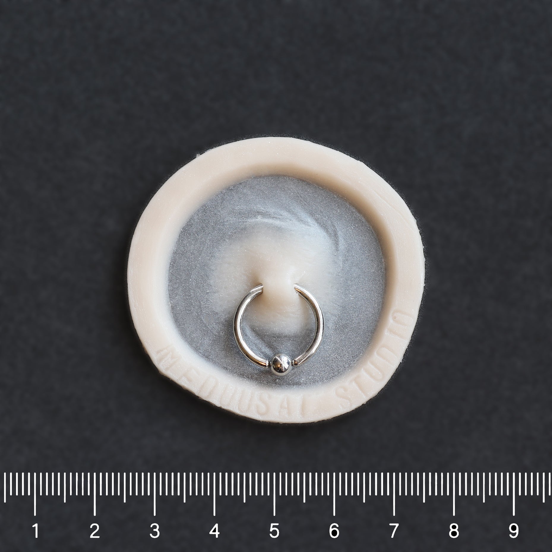 Surface Piercing - Silicone makeup prosthetic in vanilla shade on a black surface with a ruler