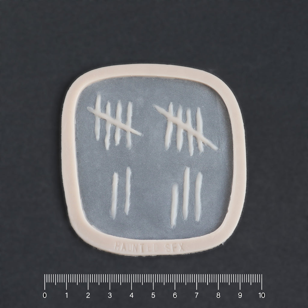 Tally Marks - Silicone makeup prosthetic in vanilla shade on a black surface with a ruler