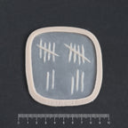 Tally Marks - Silicone makeup prosthetic in vanilla shade on a black surface with a ruler